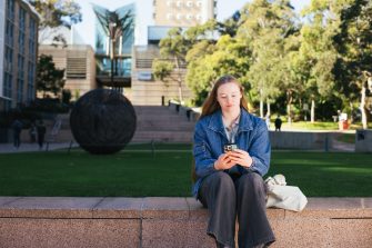 Student sitting by main walking using their phone