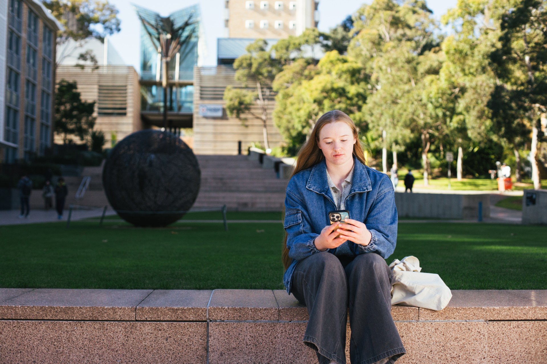 Student sitting by main walking using their phone
