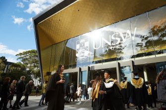 Brilliant image of sun gleaming off Sir John Clancy auditorium while happy graduates embrace.