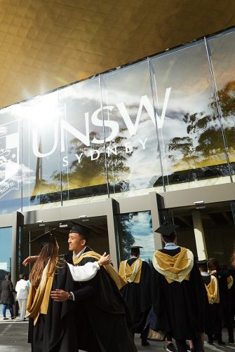 Brilliant image of sun gleaming off Sir John Clancy auditorium while happy graduates embrace.