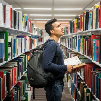 Student with backpack and open book standing between book shelves in library