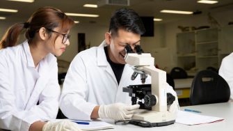 Students in Science Lab with white coat, goggles and microscopes