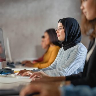 Happy Female Muslim Student Wearing a Hijab, Studying in Modern University with Diverse Multiethnic Classmates. Students Successfully Learn Computer Science, Writing Software Code.