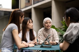 4 Students in courtyard sitting at table with ipad