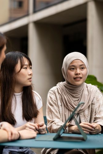 4 Students in courtyard sitting at table with ipad