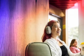 Student with headphones, holding coffee cup, looking up, colourful hair