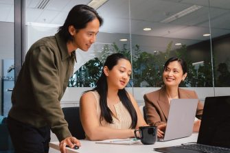 A man and two ladies in a meeting room, working on laptops