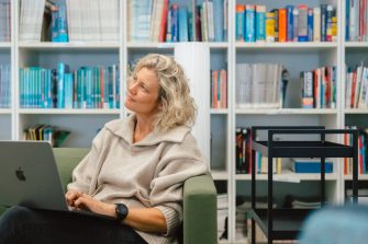 A lady in a library with her laptop thinking
