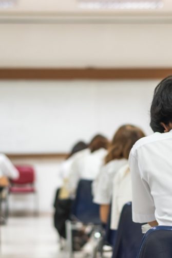 Blur school background back view university students writing answer doing exam in classroom
