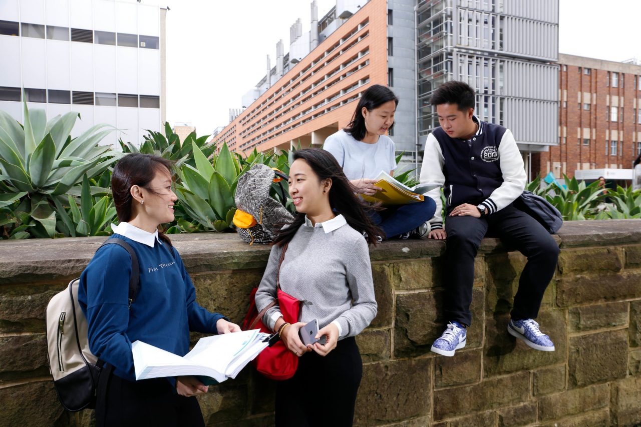 Students sitting on ledge with books and backpacks