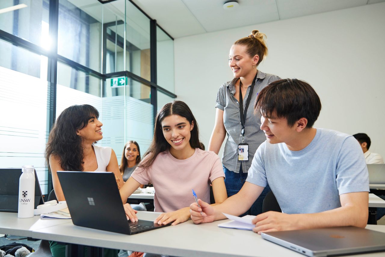 Students in classroom talking to a young staff member