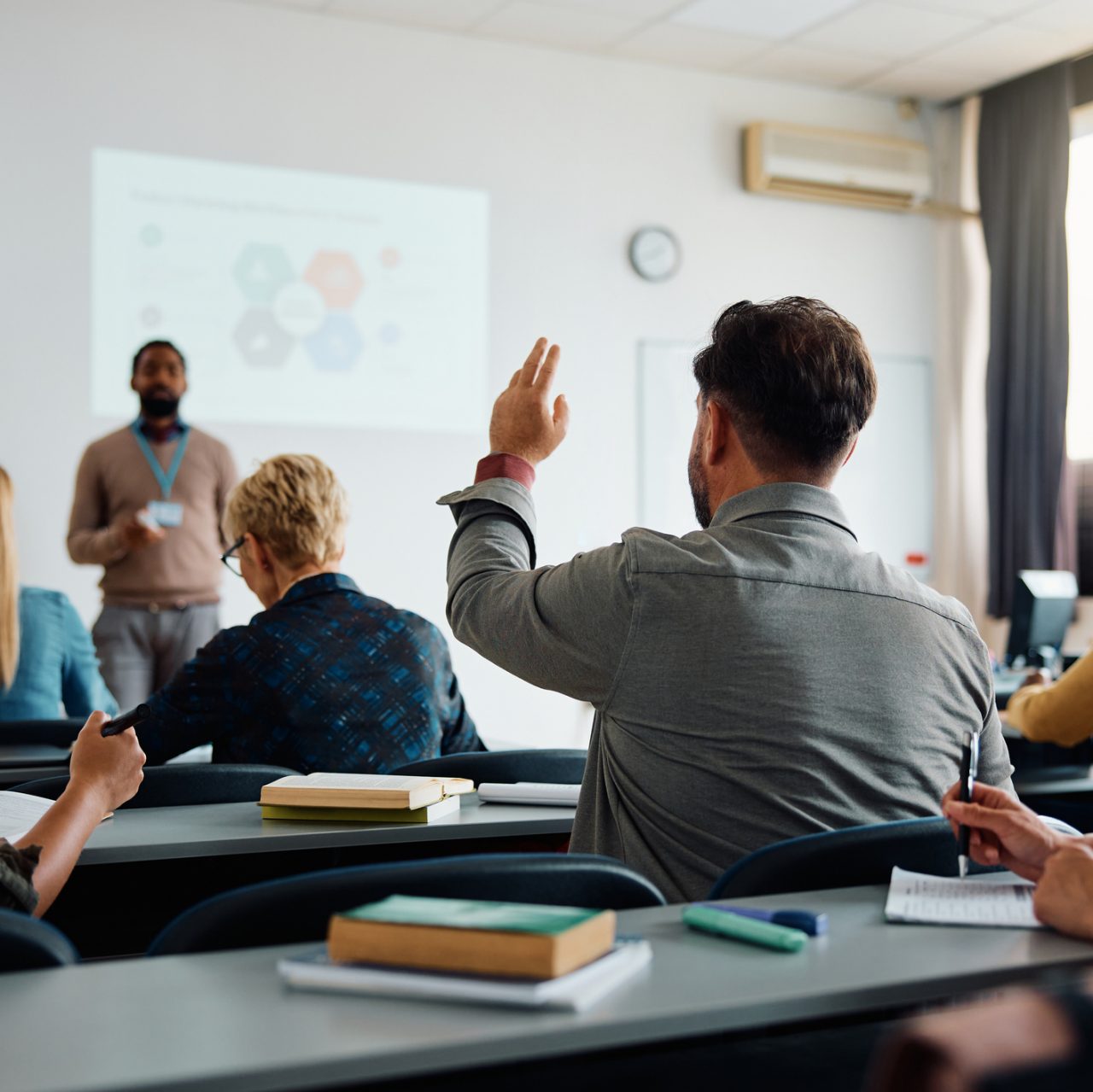 Rear view of man raising arm to ask a question during a presentation in lecture hall.