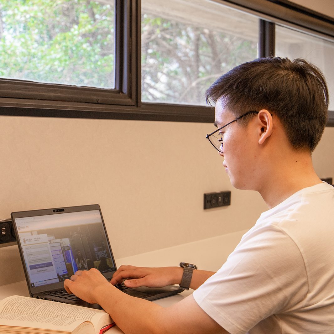 A student sitting in front of the south windows, using their laptop.
