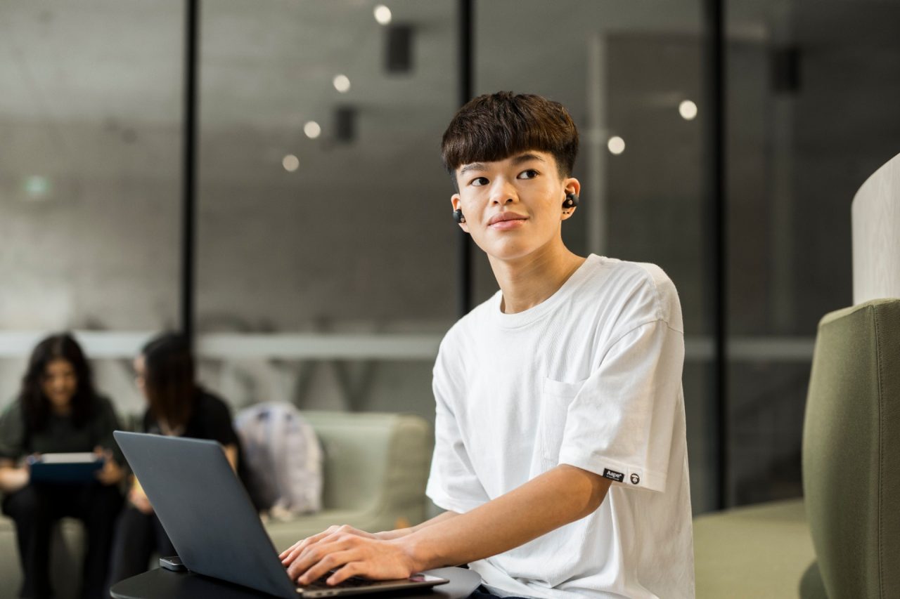 Student (Tyson) sitting in the Student Hub at L5 with headphones and laptop