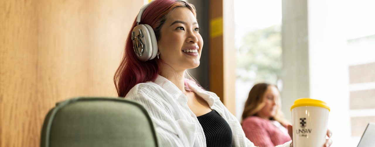 Student with headphones and coffee smiling