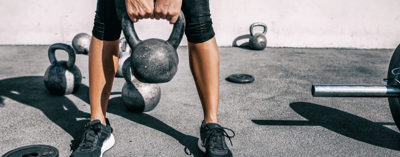 Kettlebell weightlifting athlete woman lifting weight at outdoor fitness gym. Lower body legs and feet closeup of strength training legs, glutes and back lifting free weights.