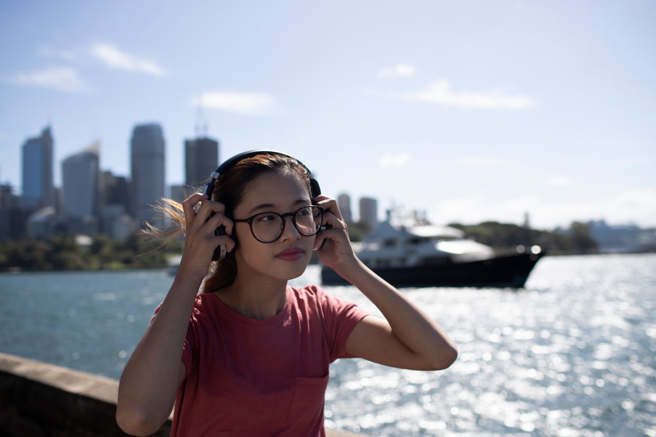 Female student putting on headphones in front of Sydney harbour skyline