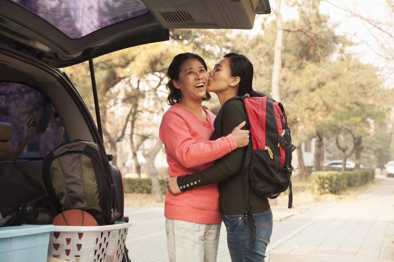 Mother and daughter embracing behind car on college campus