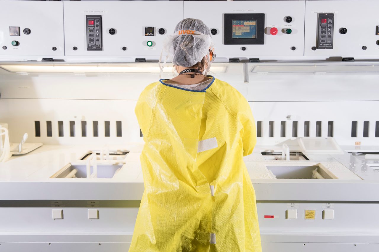 Student in lab with yellow lab coat, gloves, protective goggles and hairnet