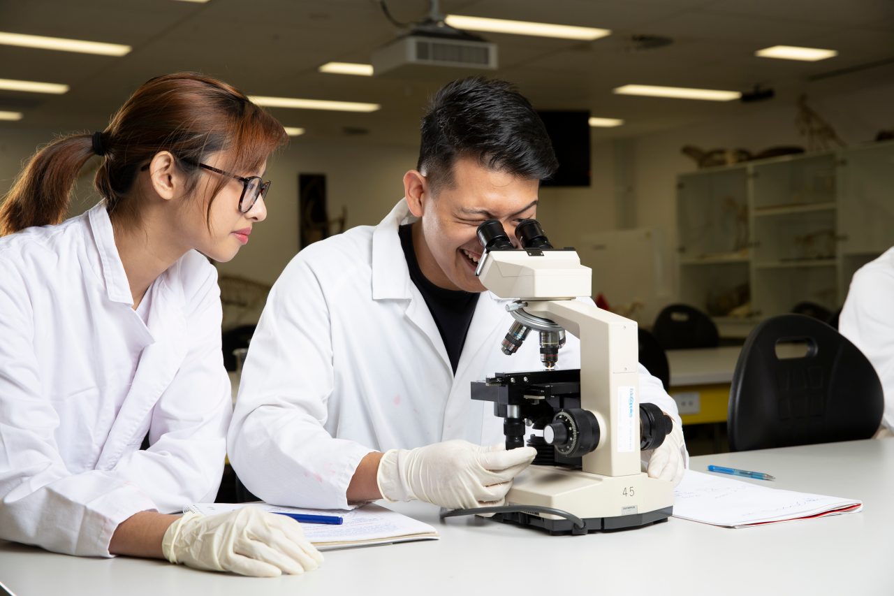 Students in Science Lab with white coat, goggles and  microscopes