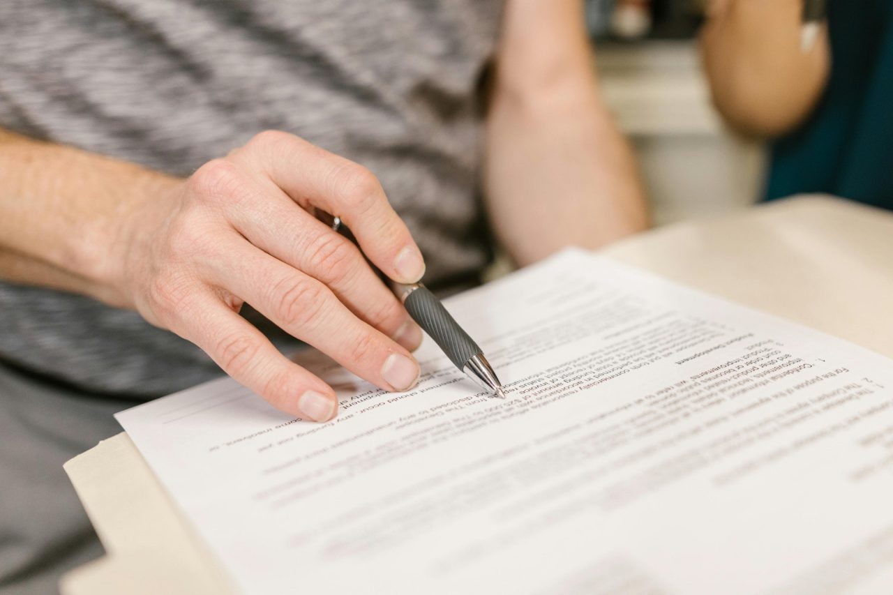 A close crop image captures a hand holding a pen, as it hovers over a contract document.